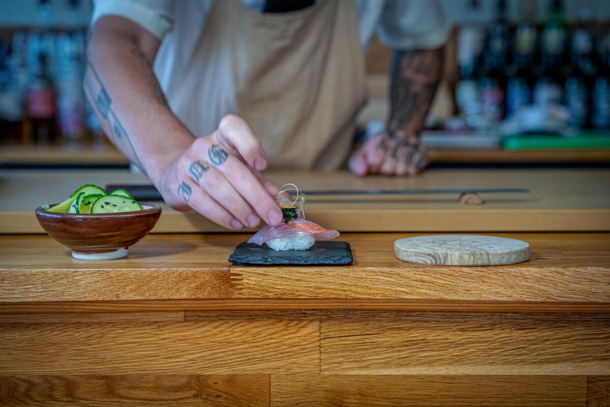 A sushi chef serves a piece of nigiri at Sushi by Scratch Restaurants.