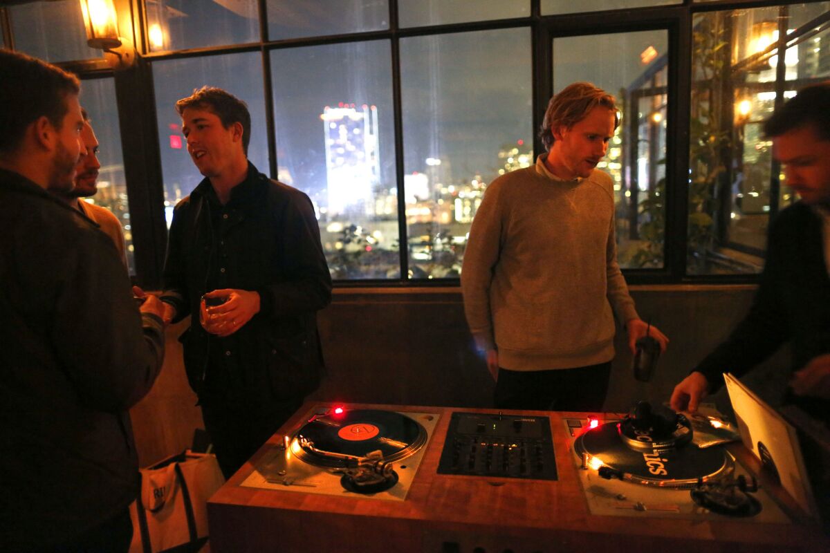 Dart DJ co-founder Jesse Kivel, left, speaks with colleagues while DJs Aaron Castle, center, and Dan Terndrup spin records during a gig at the Ace Hotel in downtown LA.