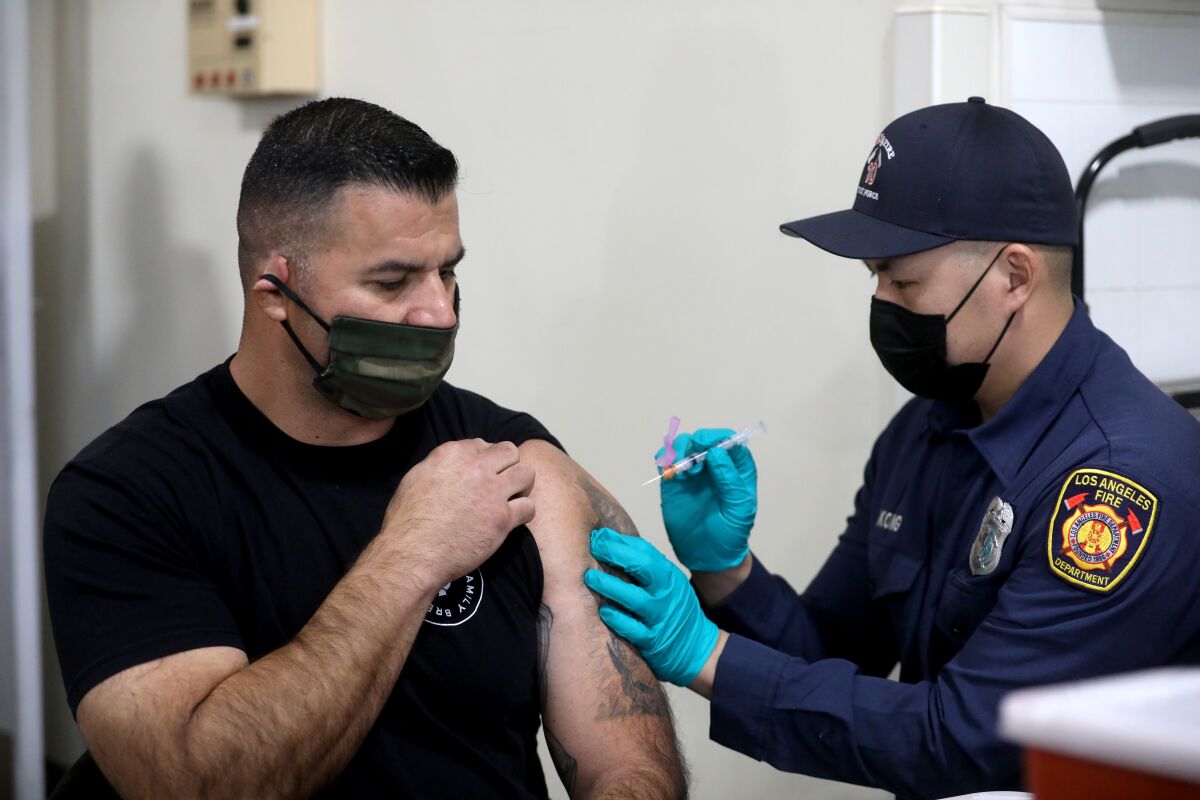 A fire department captain rolls up a sleeve to receive a COVID-19 shot. 