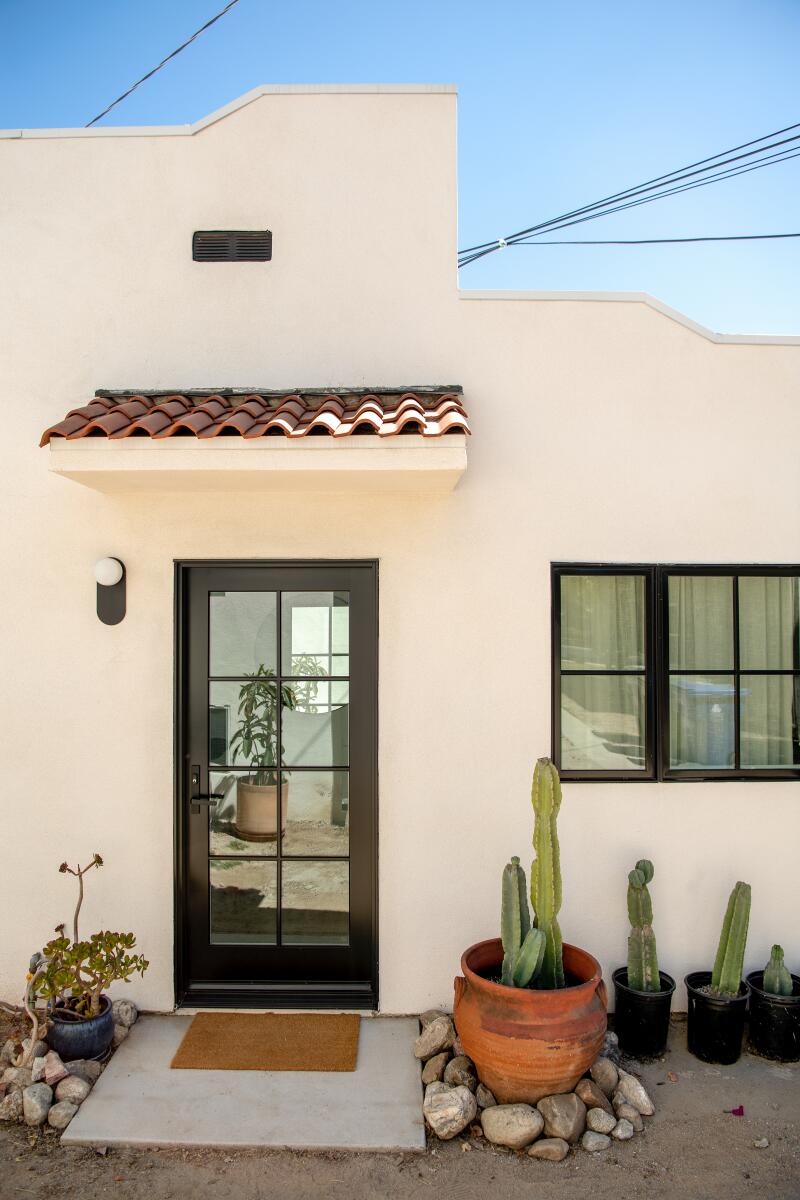 Exterior view of a Spanish-style building and its door, with potted succulents next to the door
