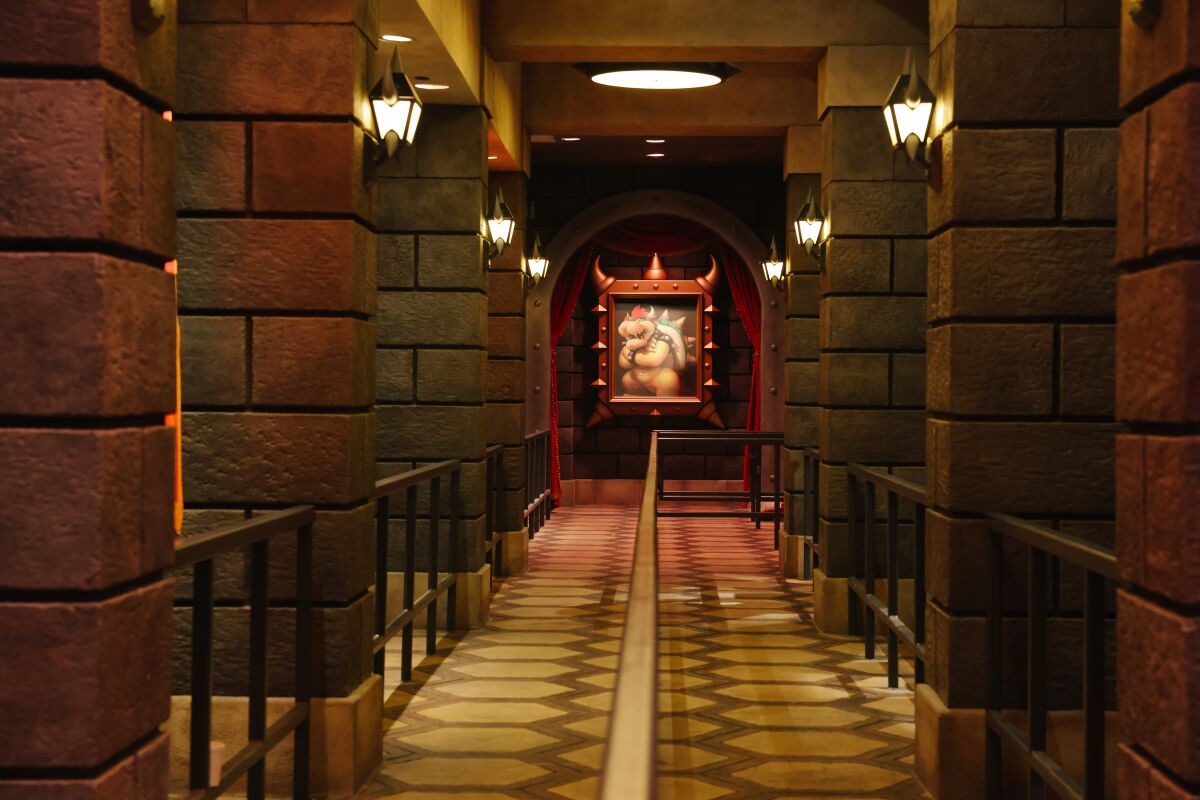 An interior waiting line is line with castle-like pillars adorned with a framed portrait of a spiked beast.