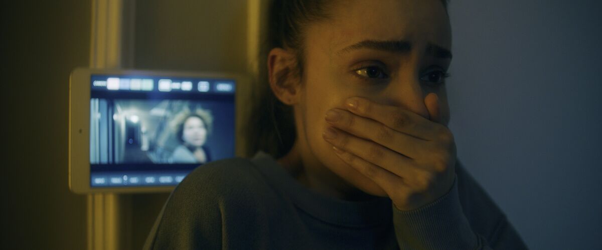 Sofia Carson stands in front of a small video screen with her hand clasped over her mouth in "Songbird."