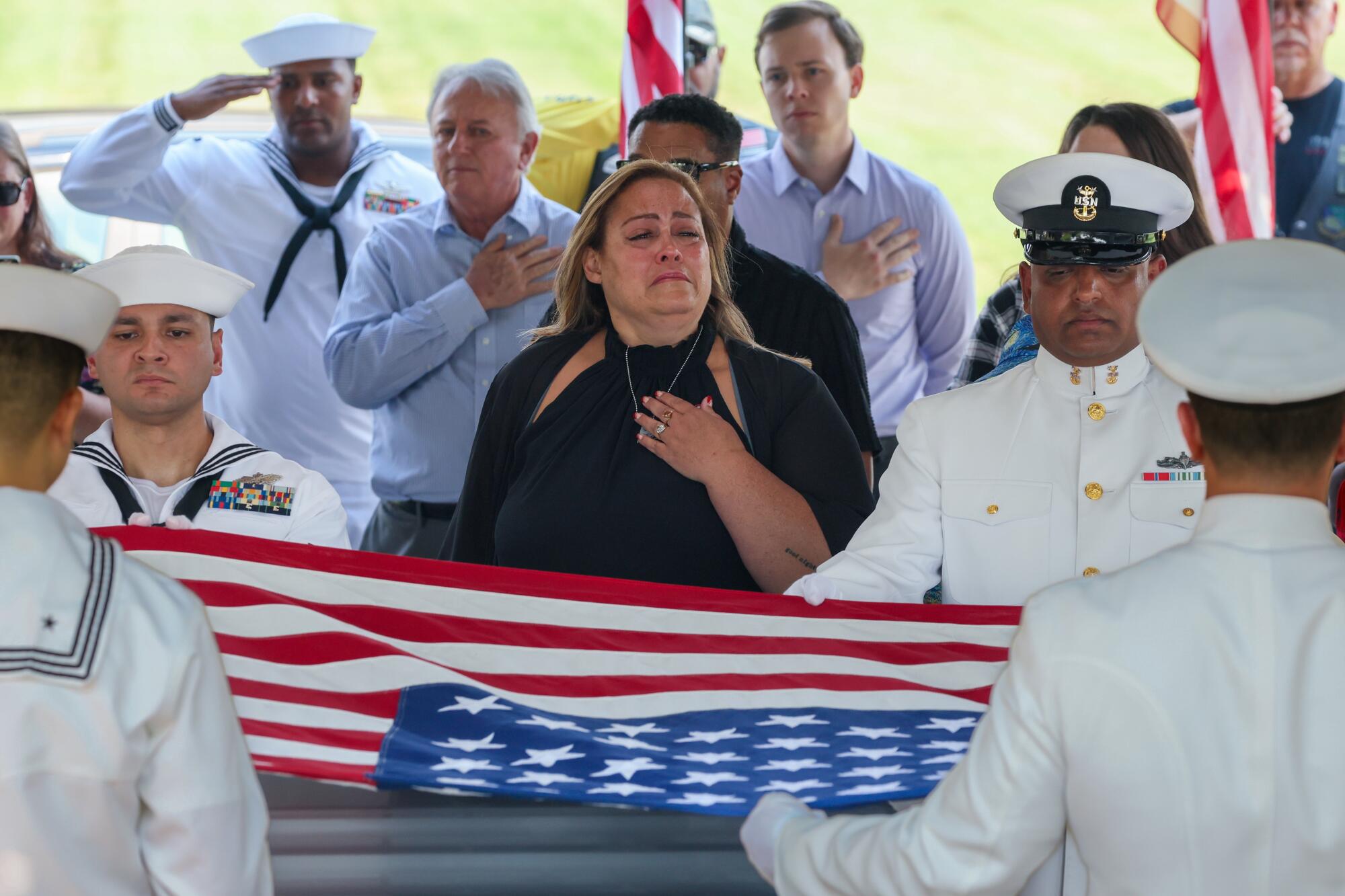 A woman in black weeps as sailors in white uniform hold a U.S. flag over a casket and other men hold a hand over their chest