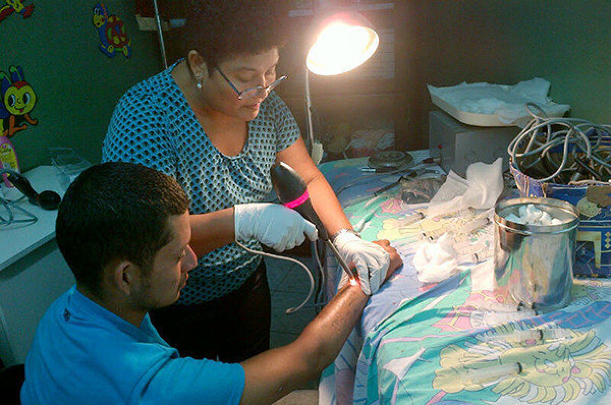 Veteran nurse Suyapa Bonilla directs infrared light onto the tattooed forearm of Osman Torres in her clinic in San Pedro Sula, Honduras. Rising gang violence has led her to limit the number of patients she sees.