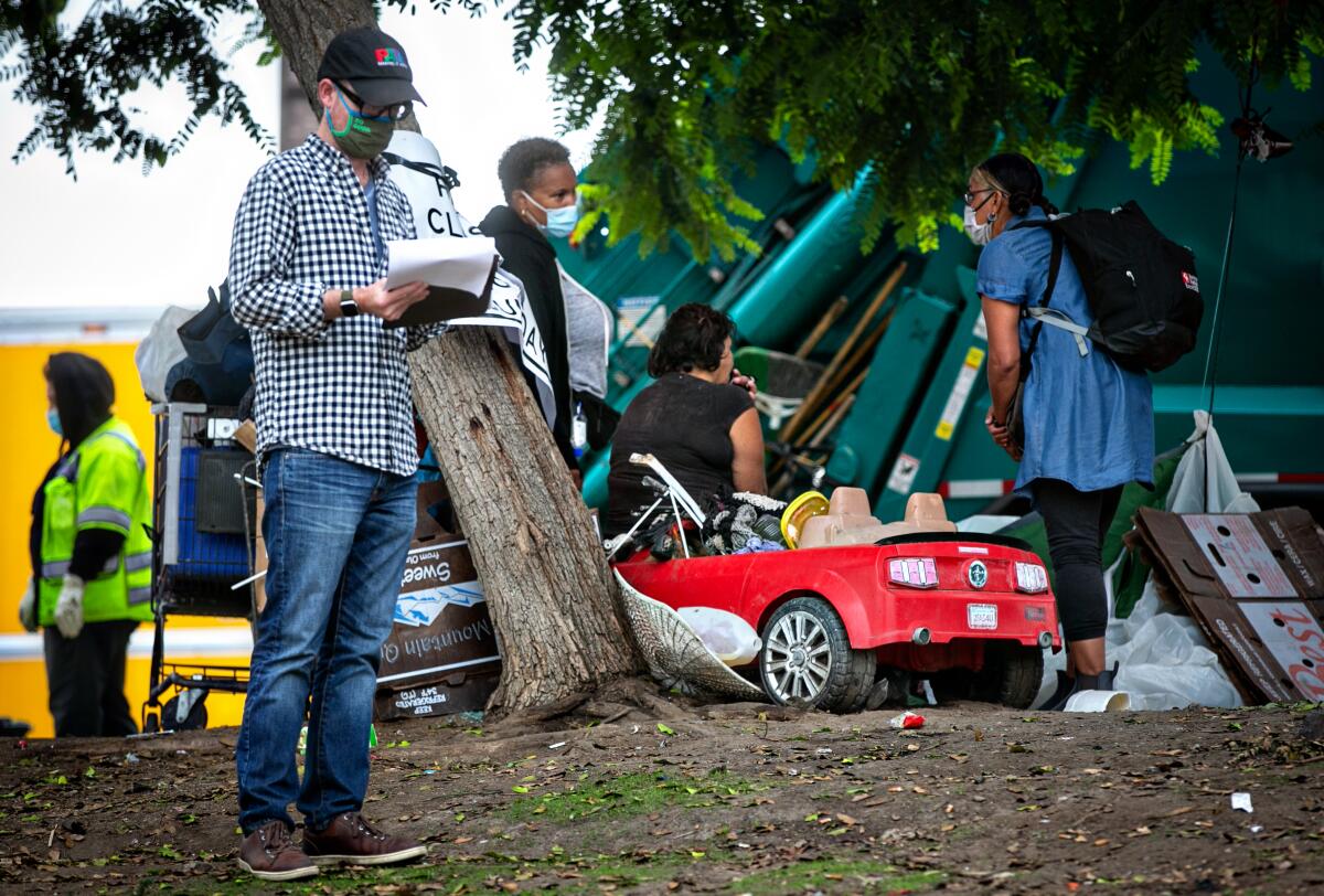 Outreach workers at a homeless encampment, with piles of garbage, belongings and a red play car