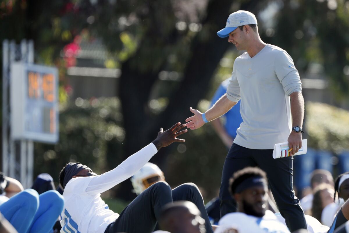 In this July 28, 2021 photo, Los Angeles Chargers head coach Brandon Staley greets wide receiver Mike Williams during practice at the NFL football team's training camp in Costa Mesa, Calif. As workers return to the office, friends reunite and more church services shift from Zoom to in person, this exact question is befuddling growing numbers of people: to shake or not to shake. (AP Photo/Alex Gallardo)