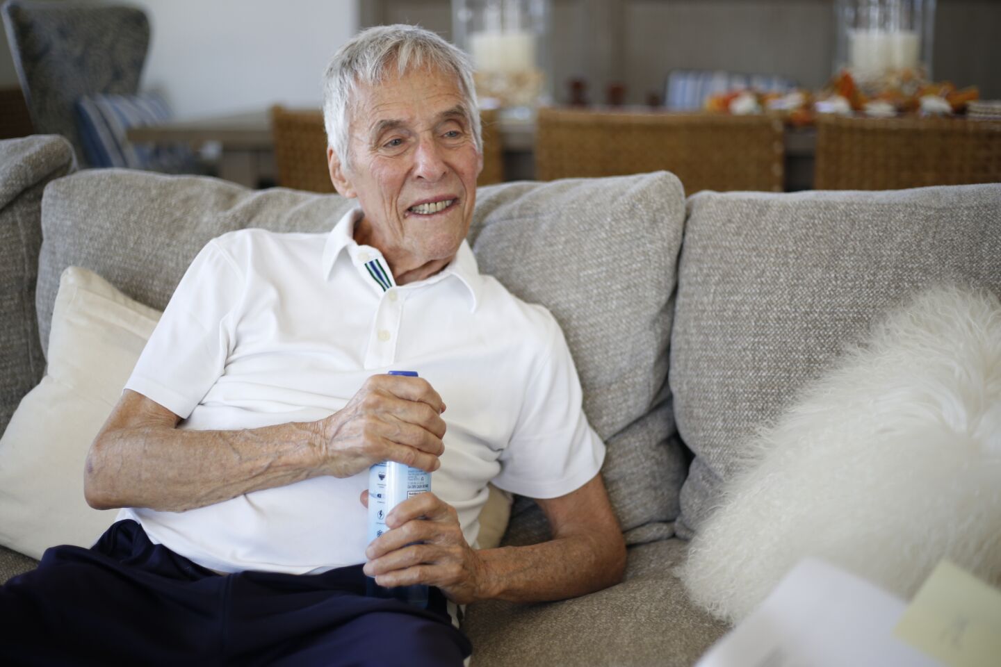 Burt Bacharach sits on a couch holding a water bottle