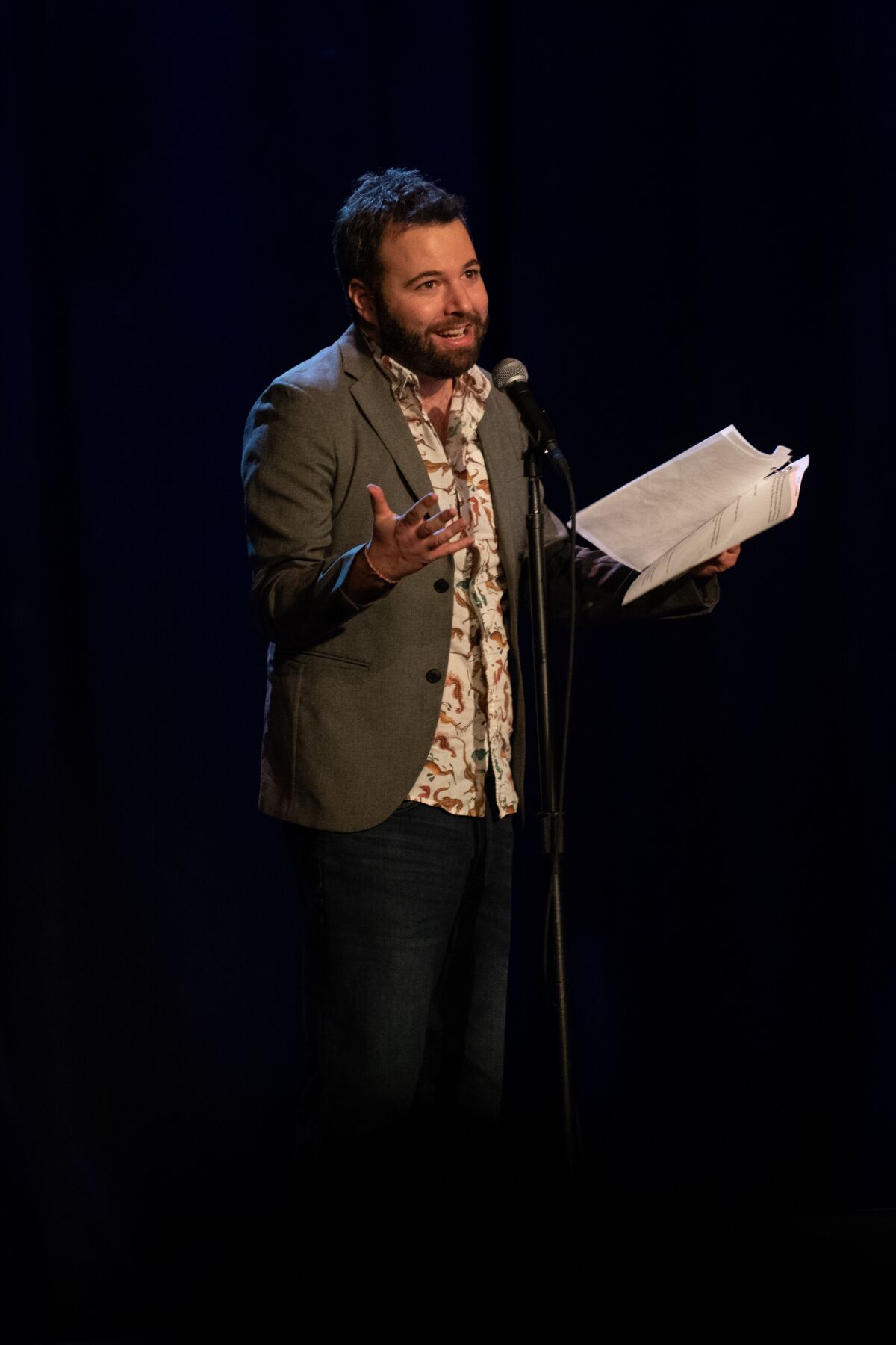 A man at a microphone holds a script.