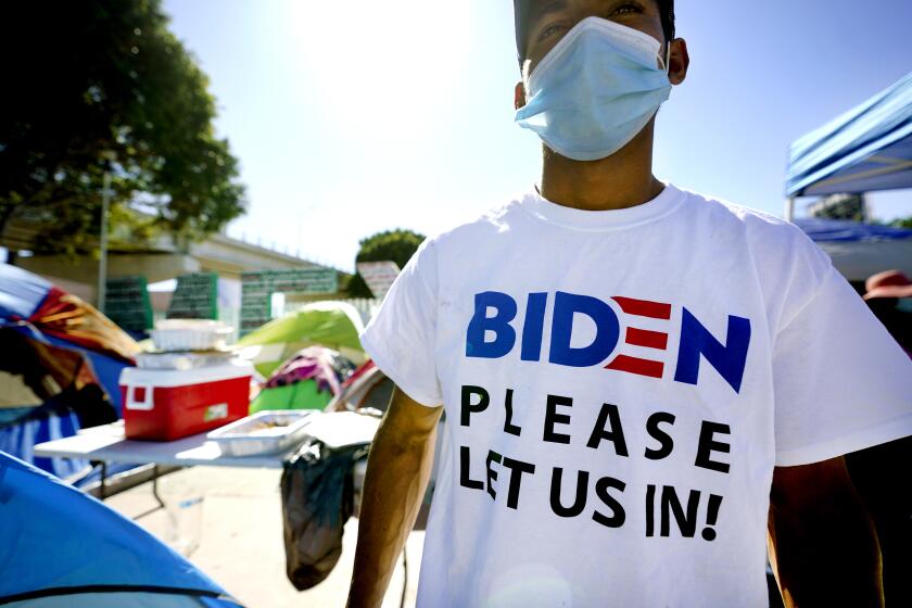 A Honduran man seeking asylum in the United States wears a shirt that reads, "Biden please let us in," as he stands among tents that line an entrance to the border crossing, Monday, March 1, 2021, in Tijuana, Mexico. President Joe Biden is holding a virtual meeting with Mexican President Andrés Manuel López Obrador. Monday's meeting was a chance for them to discuss migration, among other issues. (AP Photo/Gregory Bull)