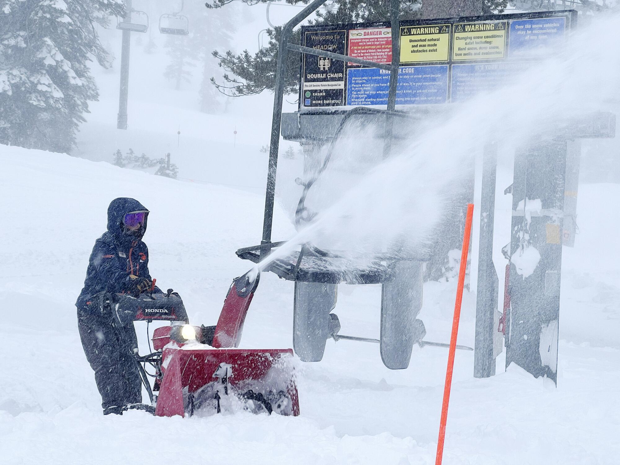 An employee uses a snowplow to remove snow at a ski resort near a ski lift.