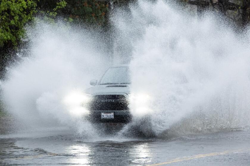 NORTH HOLLYWOOD, CA- MARCH 30: A car splashes through a flooded Vanowen Street in North Hollywood, CA on Saturday, March 30, 2024 during a rainy Easter weekend. (Myung J. Chun / Los Angeles Times)