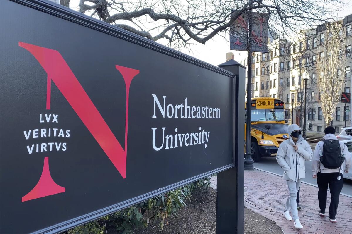 FILE - In this Jan. 31, 2019 file photo, pedestrians walk near a Northeastern University sign on the school's campus in Boston. Steve Waithe, 28, of Chicago, a former track and field coach at Northeastern University was arrested, Wednesday, April 7, 2021, and charged with using bogus social media accounts to try to trick female student-athletes into sending him nude photos of themselves, prosecutors said. (AP Photo/Rodrique Ngowi, File)