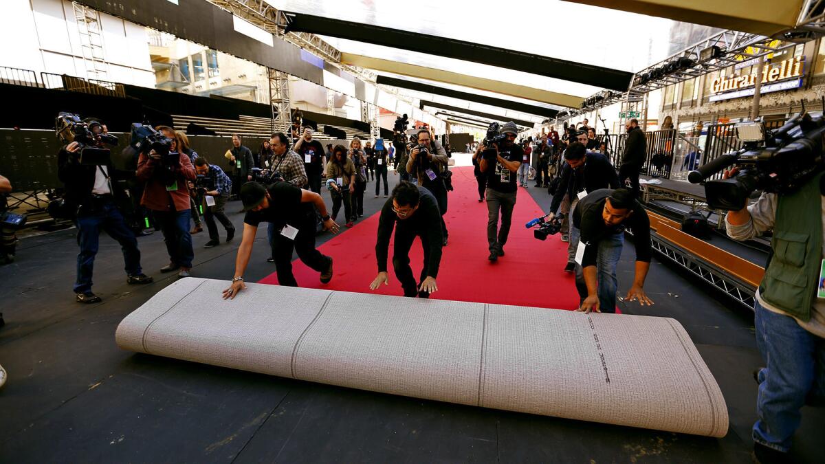 Installers maneuver a red carpet roll in front of the Dolby Theatre.