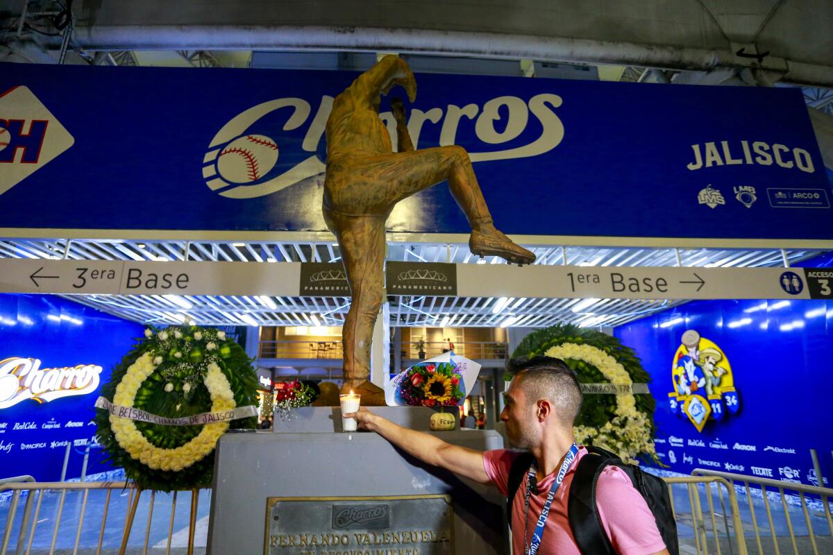 A man places a candle at the base of a statue honoring late former Dodgers pitcher Fernando Valenzuela.