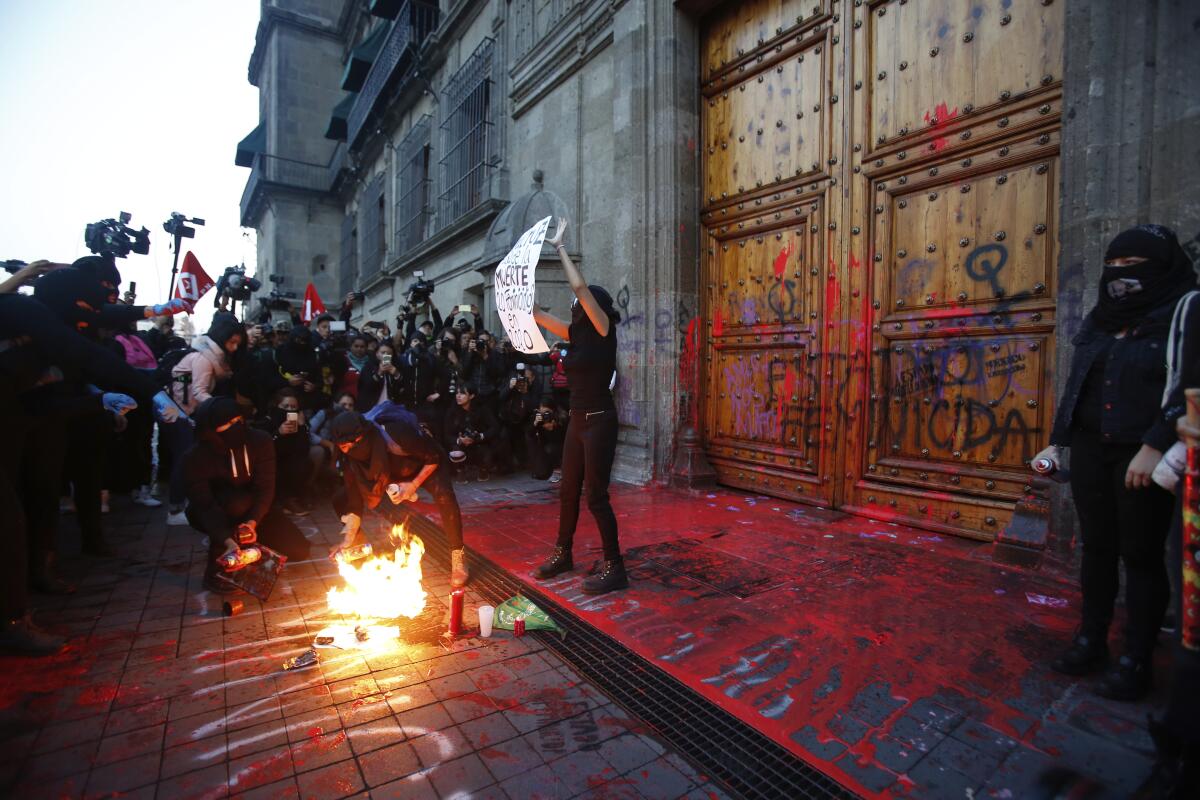 Una manifestante enmascarada que protesta contra la violencia de género se detiene con un letrero frente a los medios a la entrada de Palacio Nacional en Ciudad de México el viernes 14 de febrero de 2020. (AP Foto/Ginnette Riquelme)