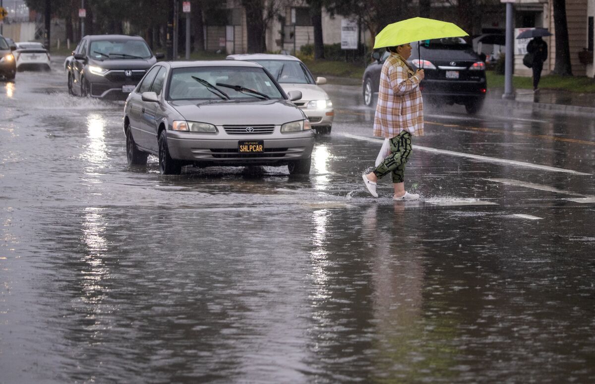 A person walks with an umbrella on a flooded street.