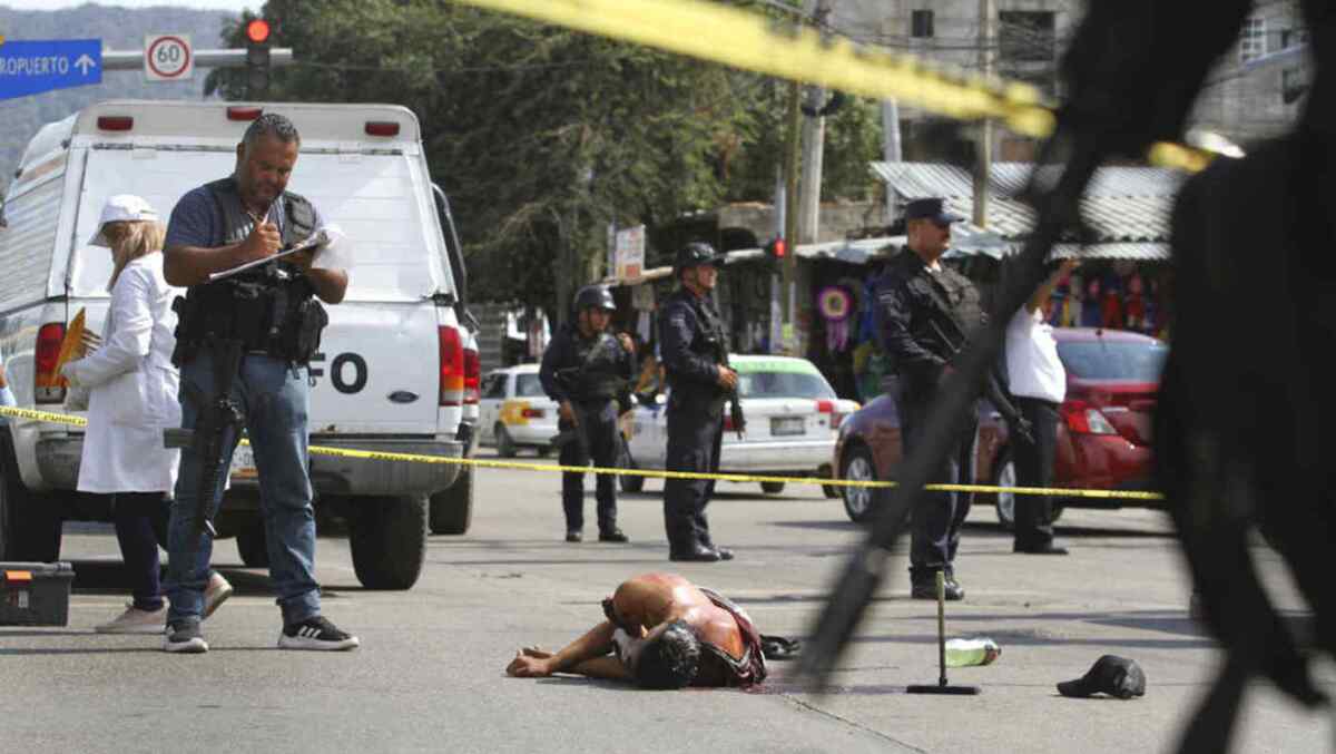 Foto del 2 de junio de 2019: el cuerpo ensangrentado de un hombre yace tendido en el medio de una calle mientras la policía y los forenses protegen la escena, en Acapulco, México.