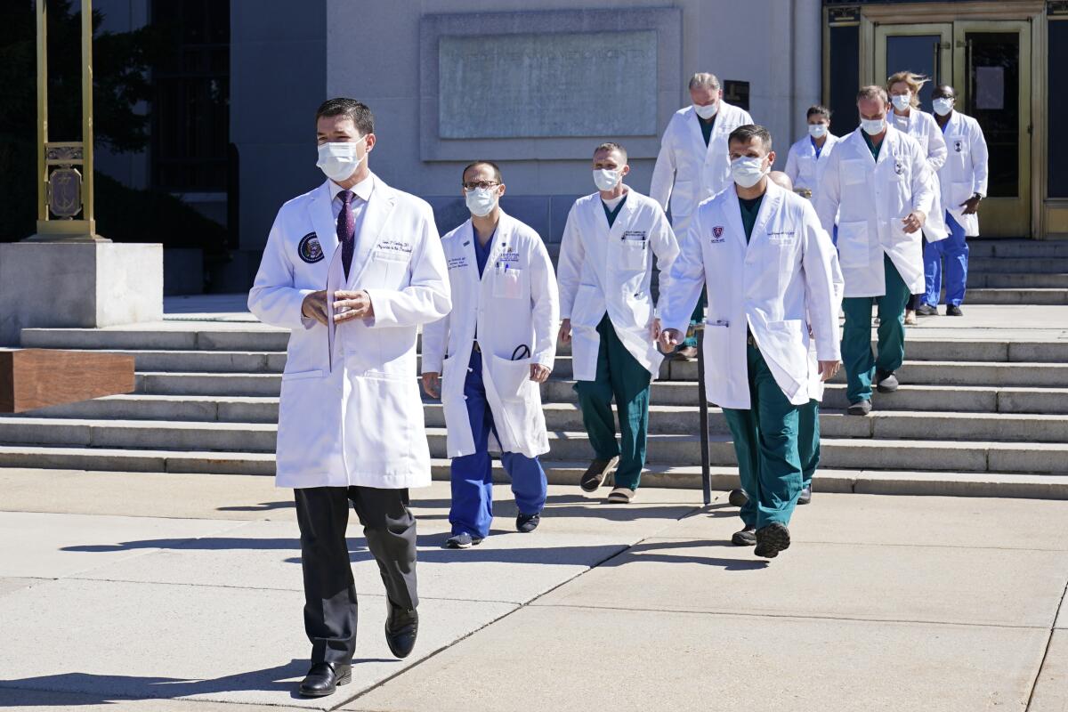 A group of doctors in white coats and masks walk down the steps of Walter Reed Medical Center.