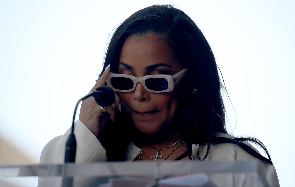 A woman dressed in white, with white sunglasses, at a microphone.