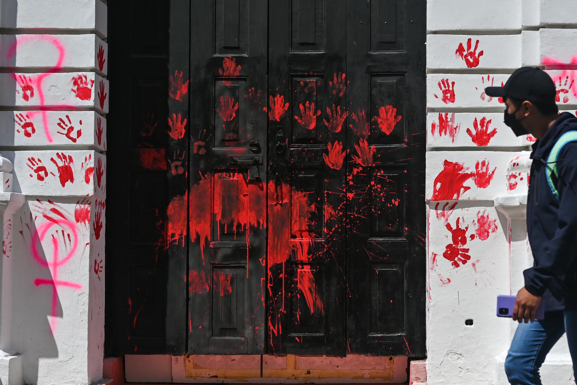 A man passes graffiti related to feminism and a vandalized front door