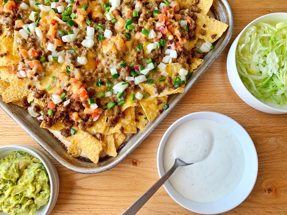 A tray of nachos next to bowls of guacamole, sour cream and shredded lettuce