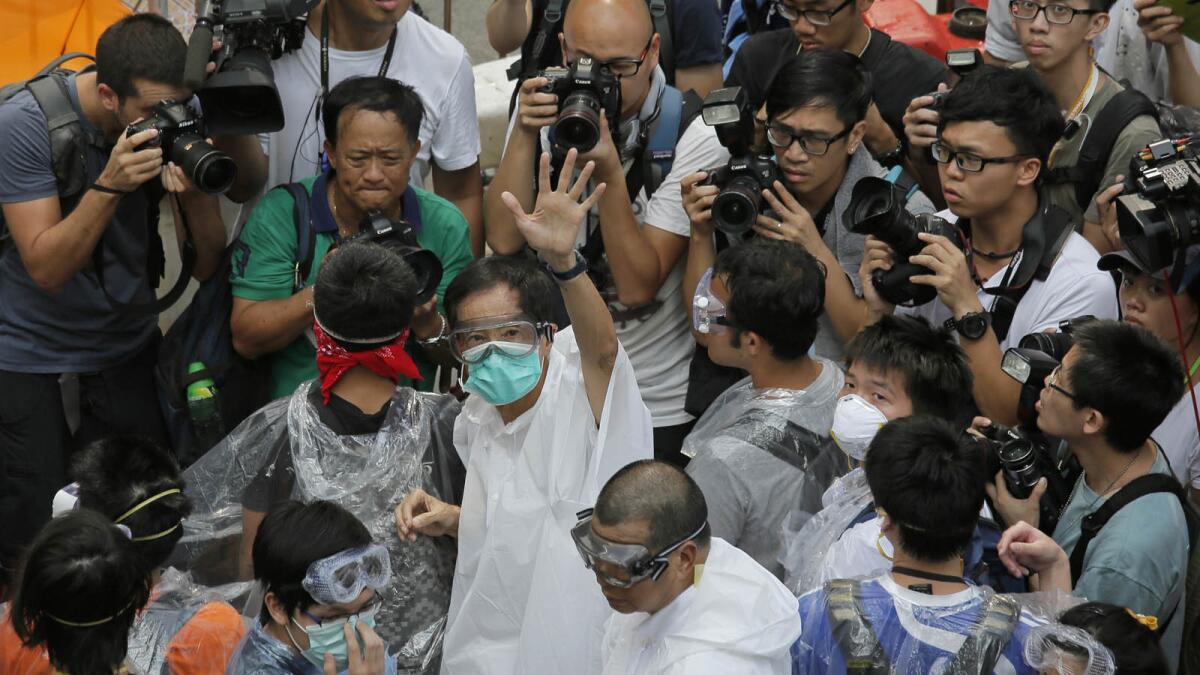 Activist Martin Lee, center, wearing goggles and a mask, waves to reporters outside government headquarters in Hong Kong.
