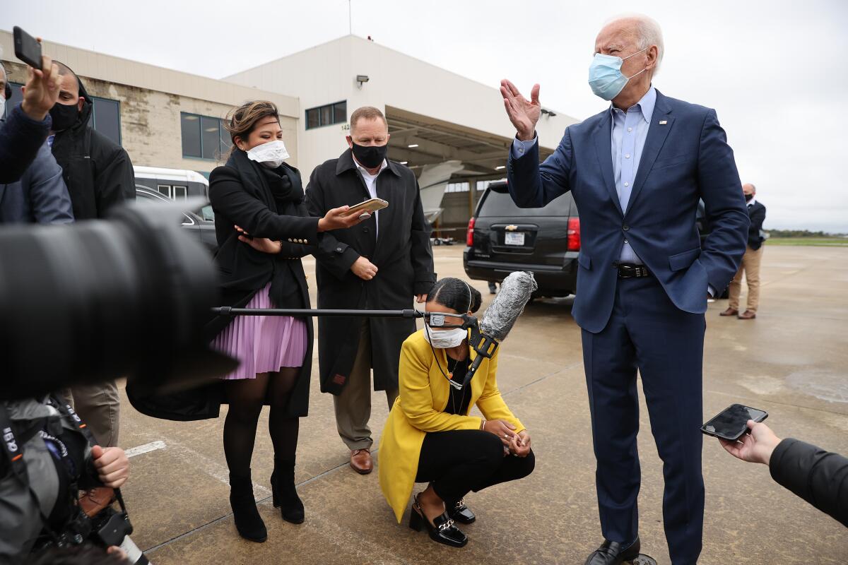 Joe Biden, masked, gestures as he talks with reporters outside a Delaware airport.