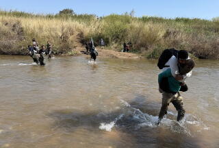 People cross a muddy river under a clear sky