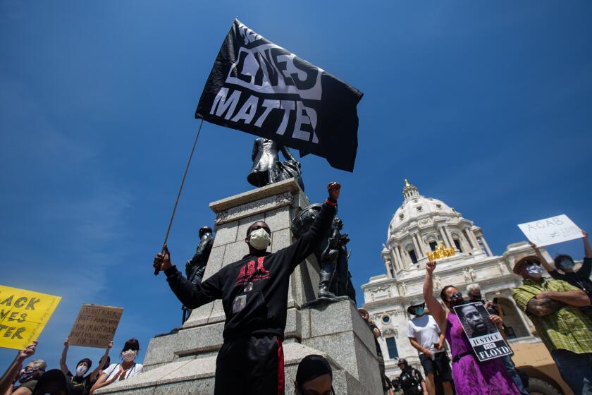 MINNEAPOLIS , MINNESOTA - MAY 31: A demonstrator stand on the steps of the Minnesota State waving a Black Lives Matters flag as thousands of protesters gather on Sunday to demand justice for George Floyd as the Minnesota National Guard secure the perimeter of the capitol building on Sunday, May 31, 2020 in Minneapolis , Minnesota. People want justice for the death of George Floyd by a police officer. (Jason Armond / Los Angeles Times)