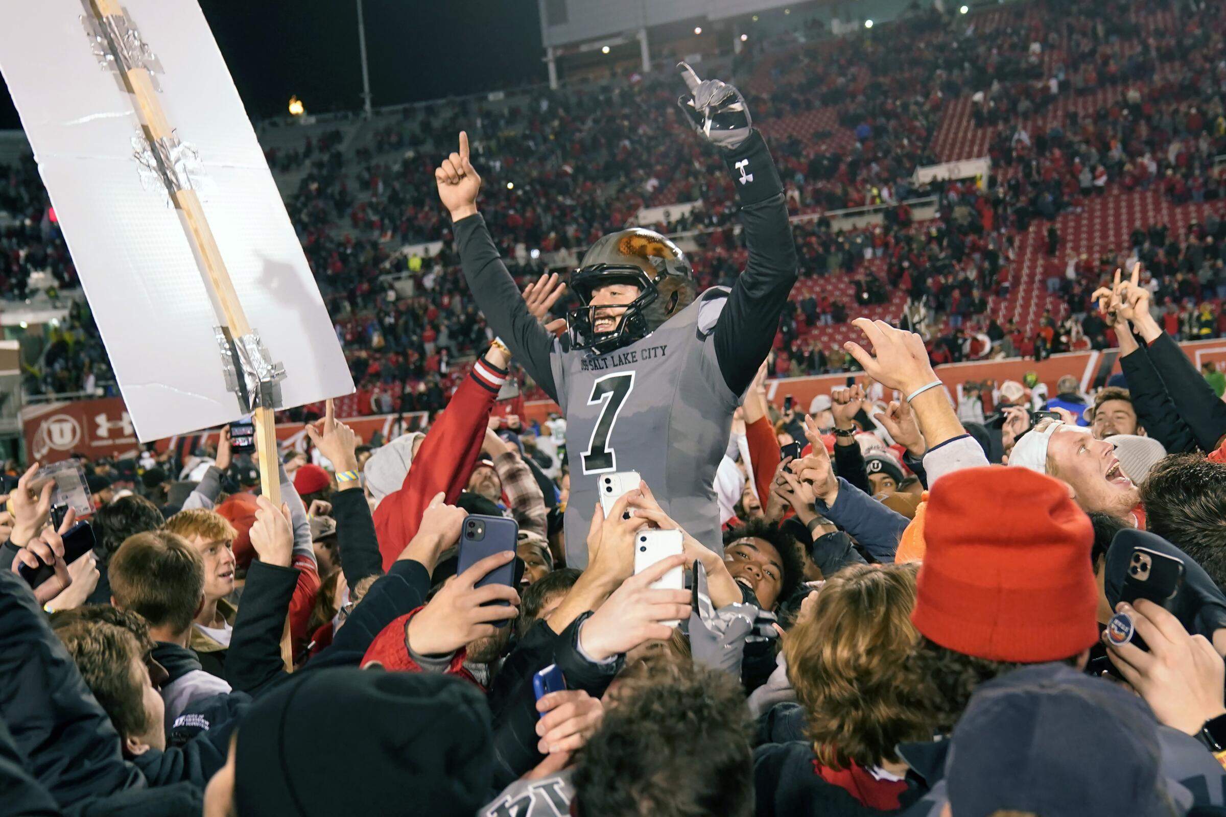 Utah quarterback Cameron Rising celebrates with students who rushed the field following the Utes' upset victory.