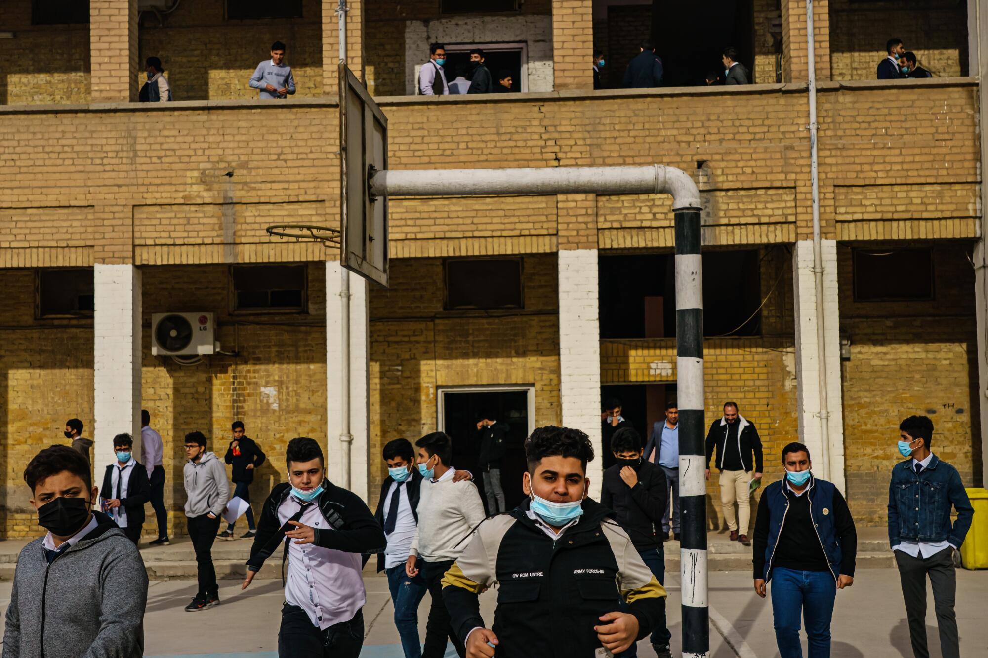Male students, some with their masks down, gather in a school courtyard