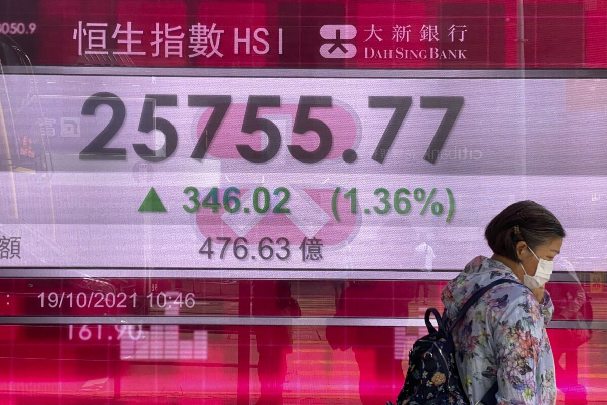 A woman walks past a bank's electronic board showing Hong Kong's Hang Seng share index in Hong Kong Tuesday, Oct. 19, 2021. Asian stock markets followed Wall Street higher as investors waited Tuesday for U.S. corporate results to see how companies are coping with supply disruptions and the past quarter's surge in coronavirus infections. (AP Photo/Vincent Yu)