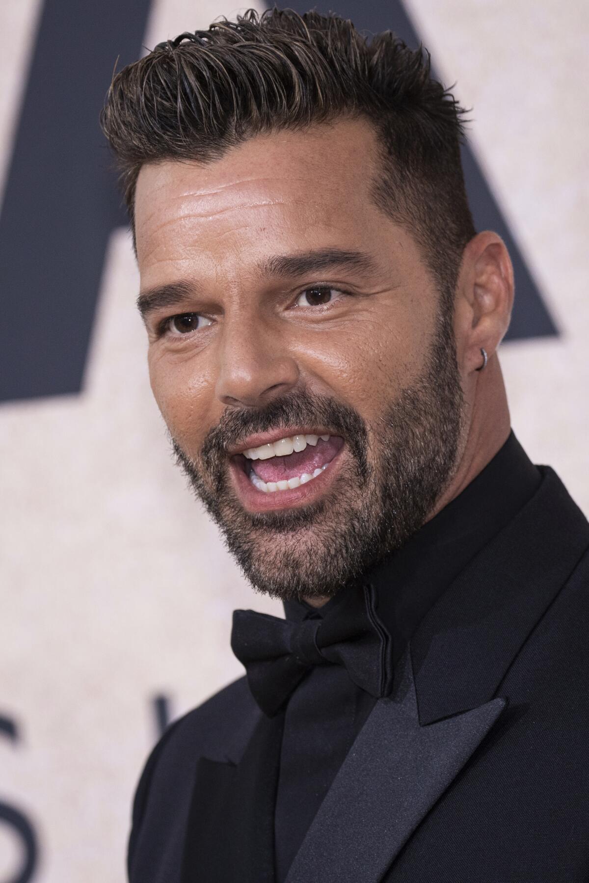 Ricky Martin poses and smiles wearing a black tuxedo, shirt and bow tie