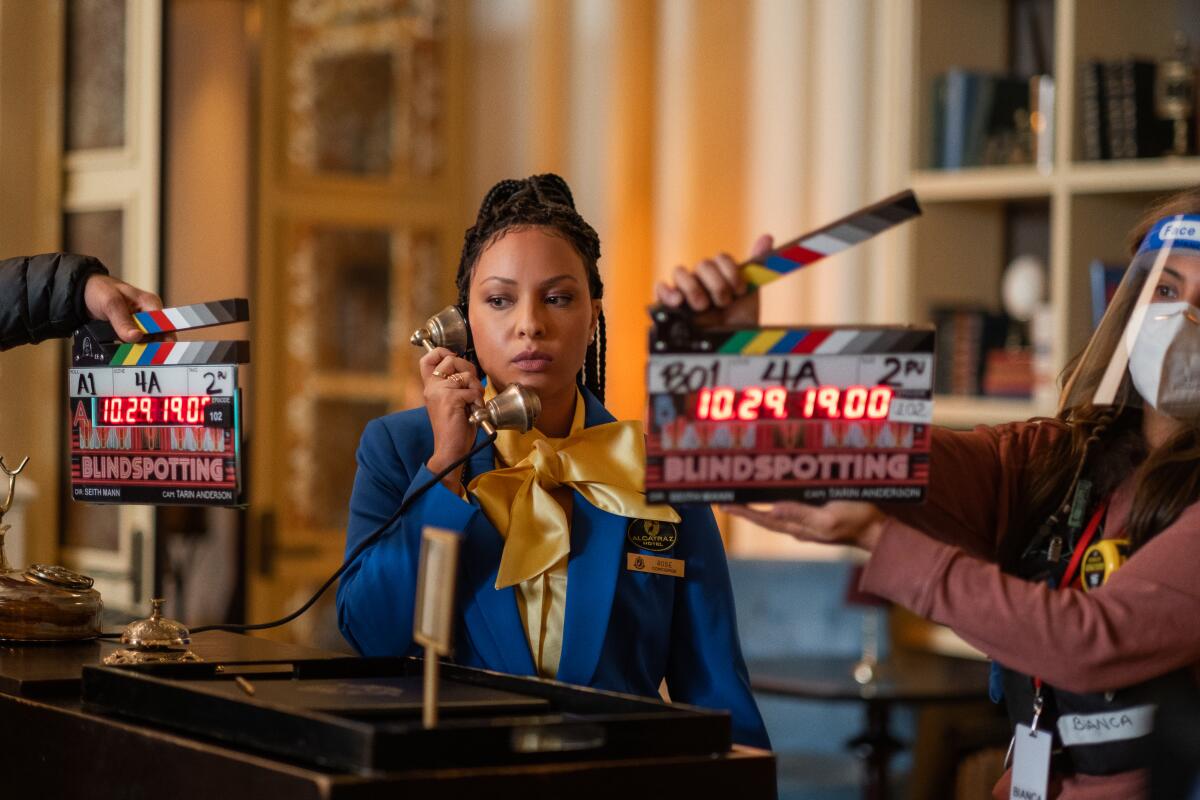 A woman dressed as a hotel receptionist on a TV set, her face framed by slates.