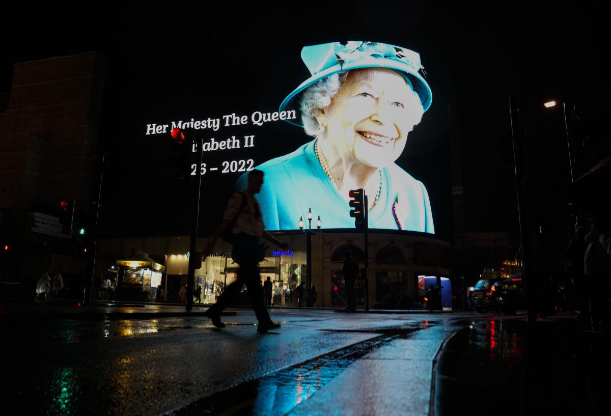 A man walks with an umbrella past an image of Queen Elizabeth II at Piccadilly Circus.