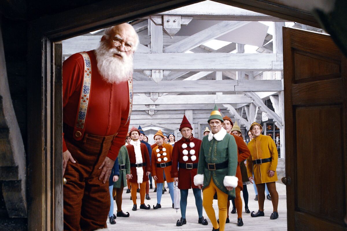 Santa and a group of elves peer through a door.