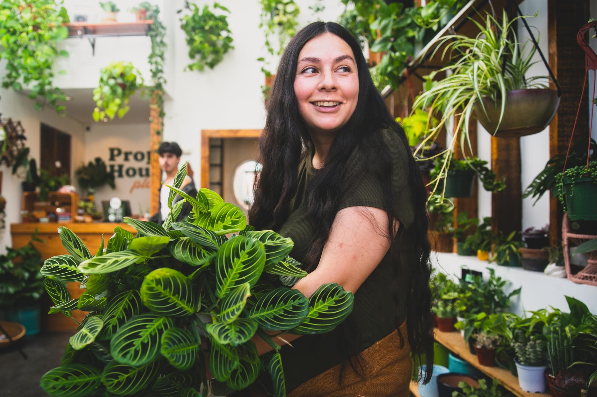 Young woman with long dark hair smiling holding a green plant.