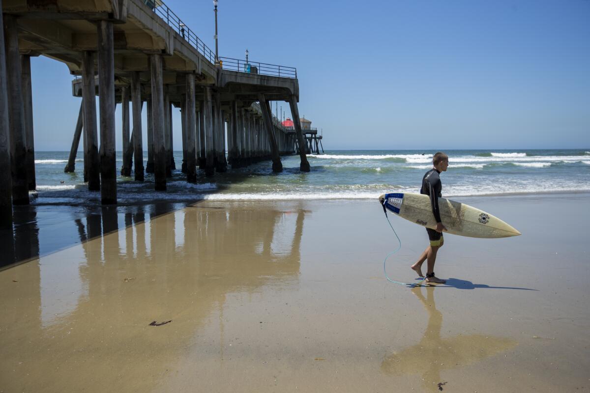 A surfer walks near the pier in Huntington Beach on May 5.