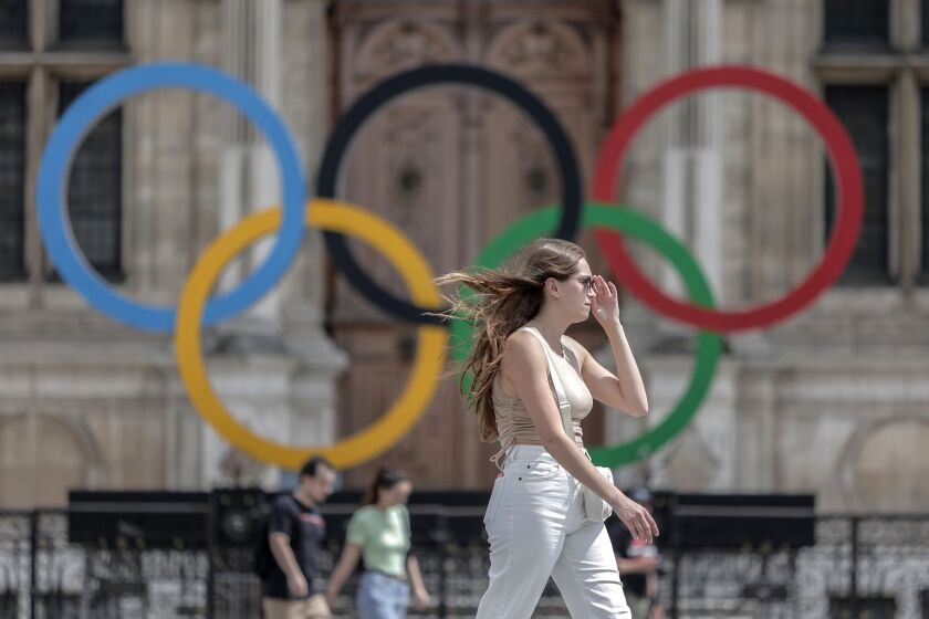 FILE - A woman passes by the Olympic rings at the City Hall in Paris, on July 25, 2022. Latvia is threatening to boycott next year’s Paris Olympics if athletes from Russia and its ally Belarus are allowed to take part after Russia's invasion of Ukraine. (AP Photo/Lewis Joly, File)