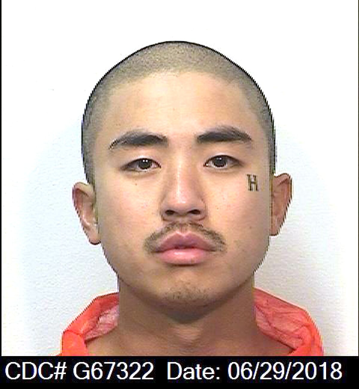A mug shot of a man in an orange prison jumpsuit, with a tattoo of an H near his left eye