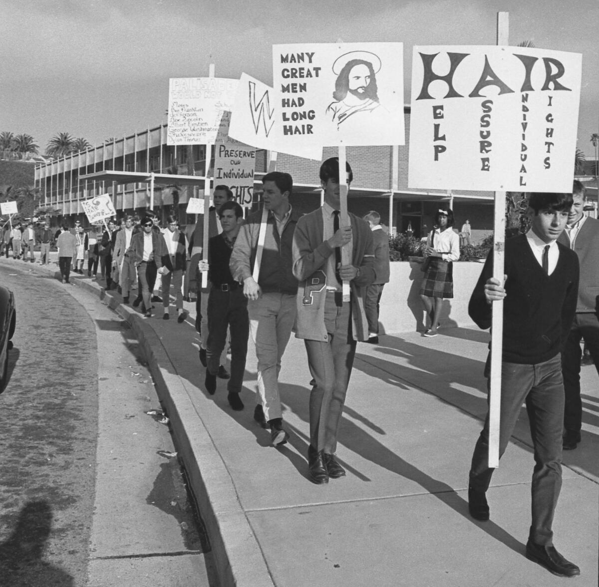 Young people carrying signs walk in line along a sidewalk.
