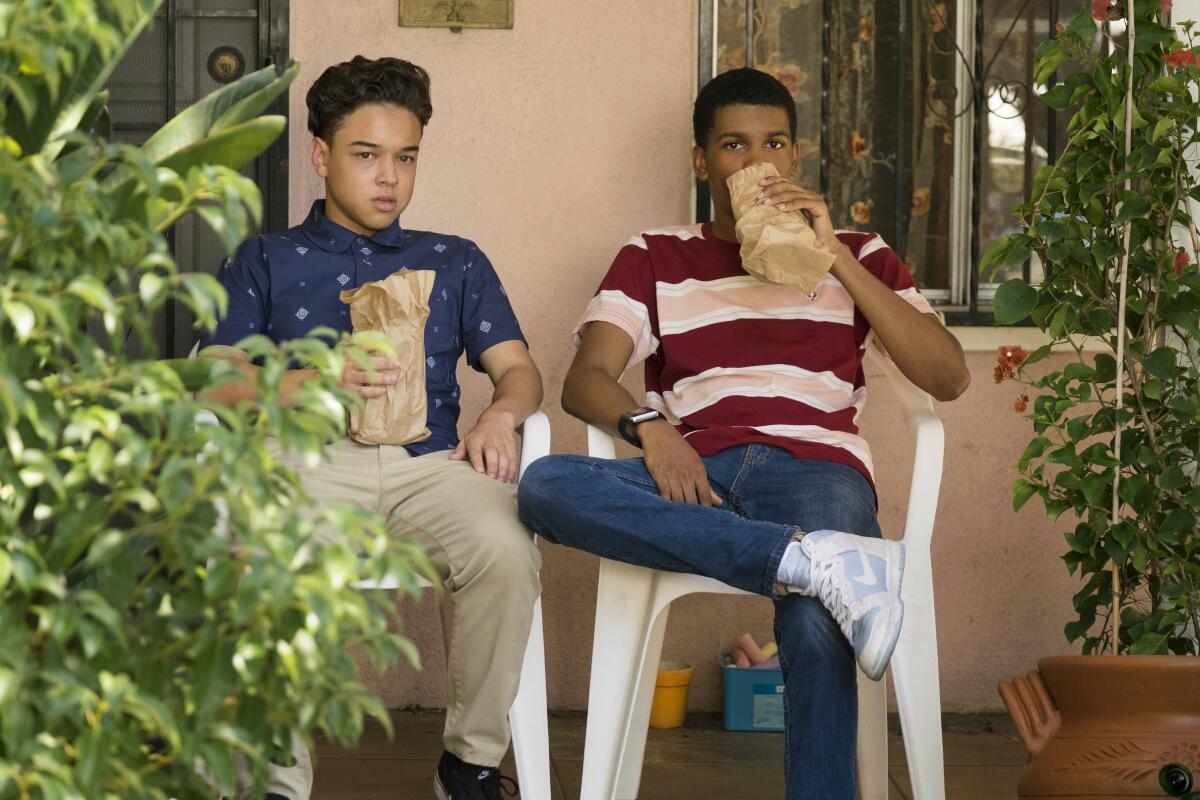 Two teen boys drink out of paper bags on a porch. 
