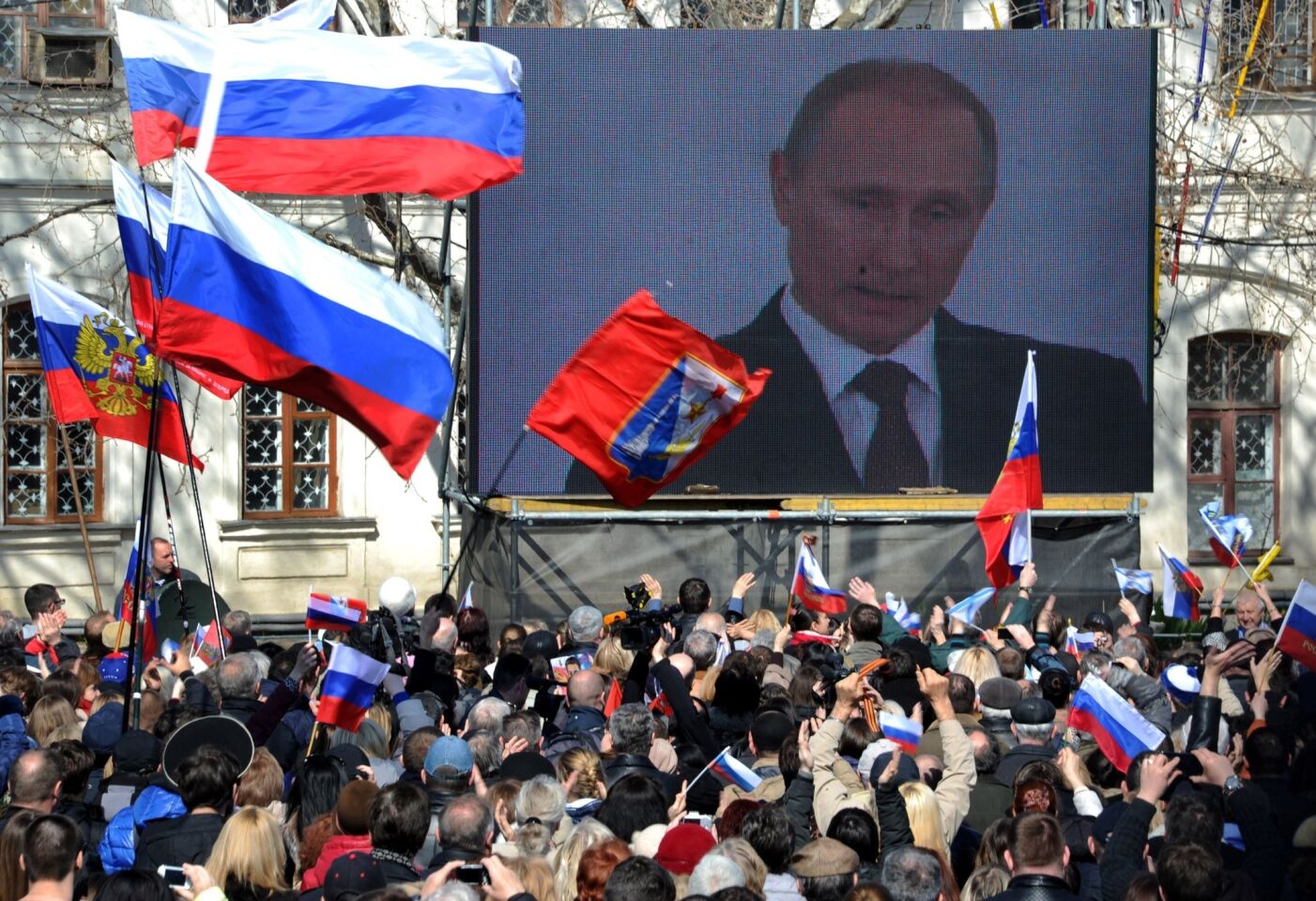 People wave flags as they watch Russian President Vladimir Putin deliver a speech in the Crimean city of Sevastopol.