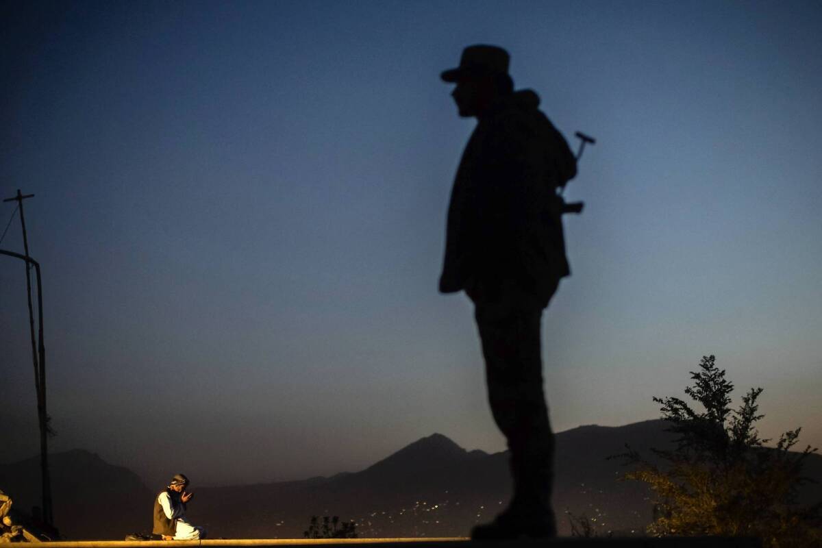 An Afghan police officer keeps an eye out while a man prays on a hilltop in Kabul.