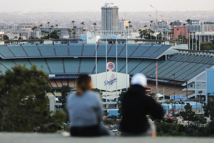 LOS ANGELES, CALIFORNIA - MARCH 26: People sit on a hill overlooking Dodger Stadium on what was supposed to be Major League Baseball's opening day, now postponed due to the coronavirus, on March 26, 2020 in Los Angeles, California. The Los Angeles Dodgers were slated to play against the San Francisco Giants at the stadium today. Major League Baseball Commissioner Rob Manfred recently said the league is "probably not gonna be able to" play a full 162 game regular season due to the spread of COVID-19. (Photo by Mario Tama/Getty Images)