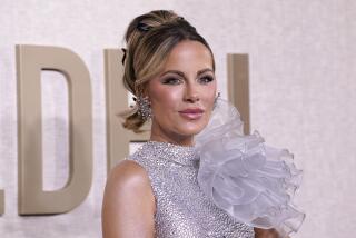 Kate Beckinsale poses, smiles with hair up while wearing silver gown covered in rhinestone with a fluffed shoulder piece