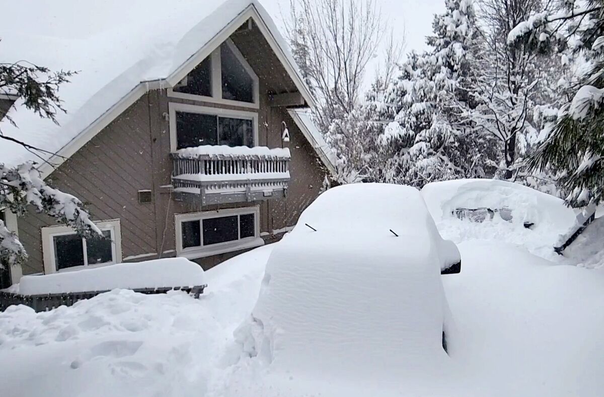 A parked car in front of a mountain home is buried in snow