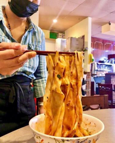 Biang biang noodles held aloft over a bowl with chopsticks