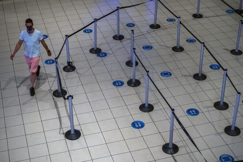 A man in a mask walks in an empty airport terminal