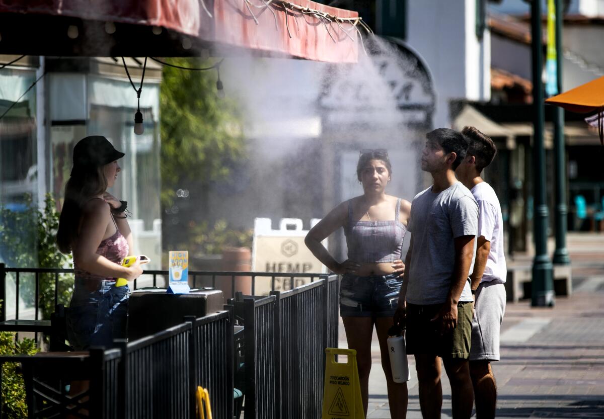 A group of people stand under a device spraying mist on a sidewalk.